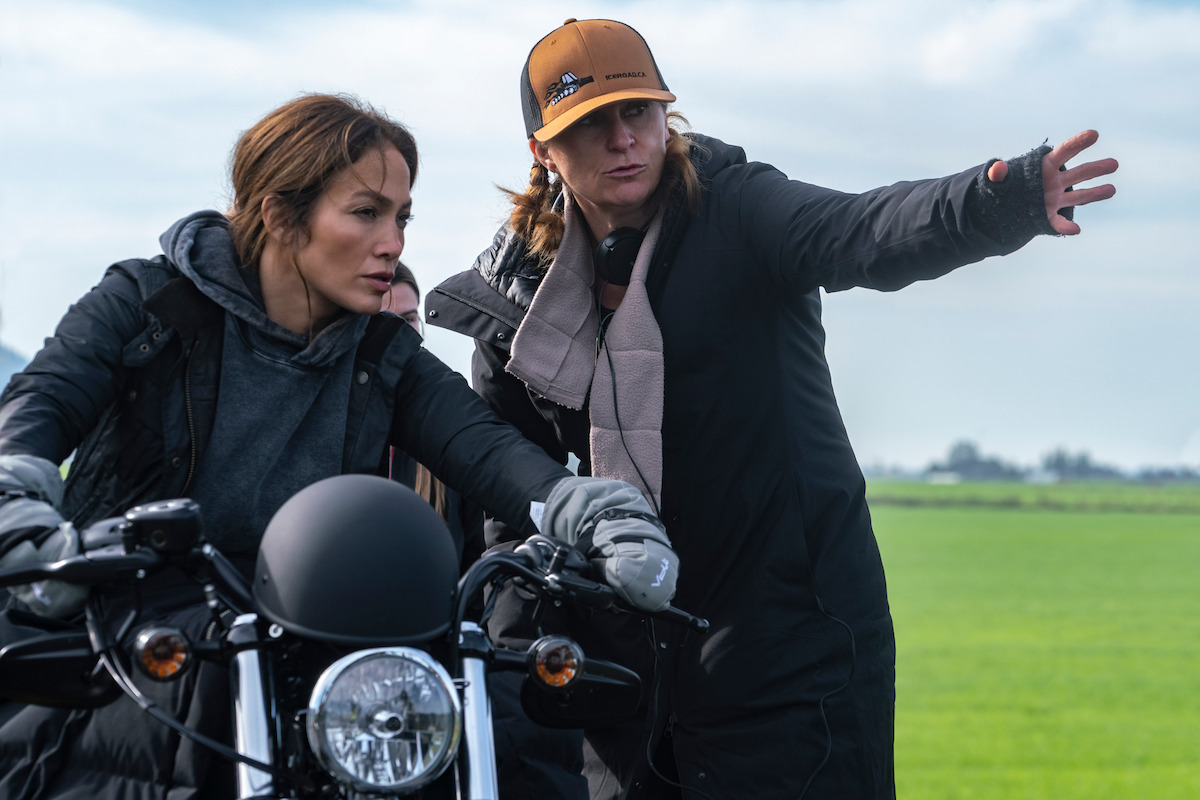 Jennifer Lopez sits astride a motorcycle as Niki Caro stands beside her and points into the distance in a behind-the-scenes still from ‘The Mother.’