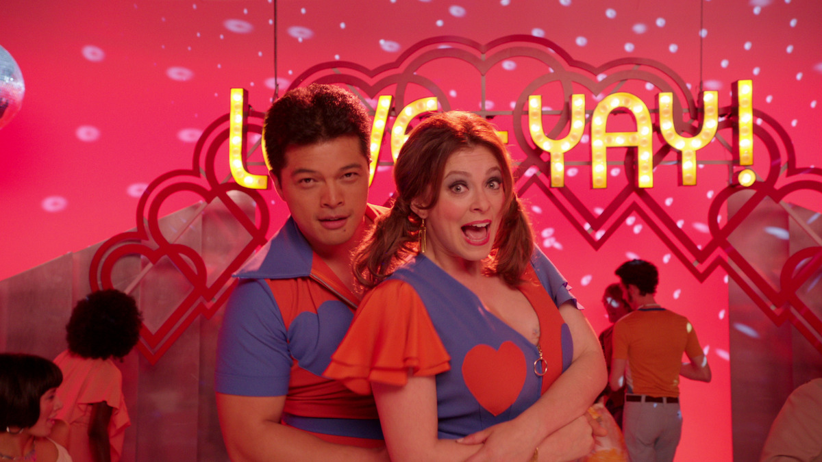  Rebecca and Josh appear in heart-spangled ’70s getups to sing about love’s alleged ability to solve all of life’s troubles