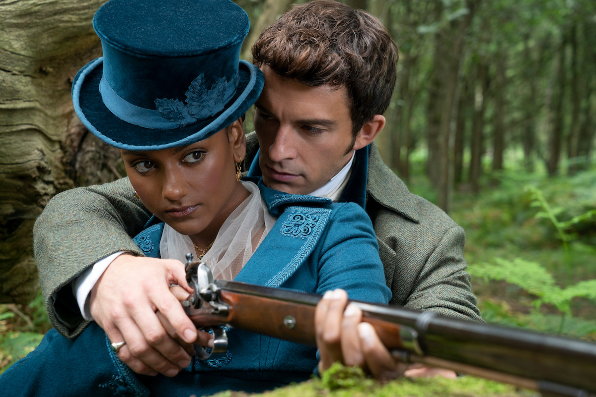 Anthony (Jonathan Bailey) shows Kate (Simone Ashley) how to aim a rifle.