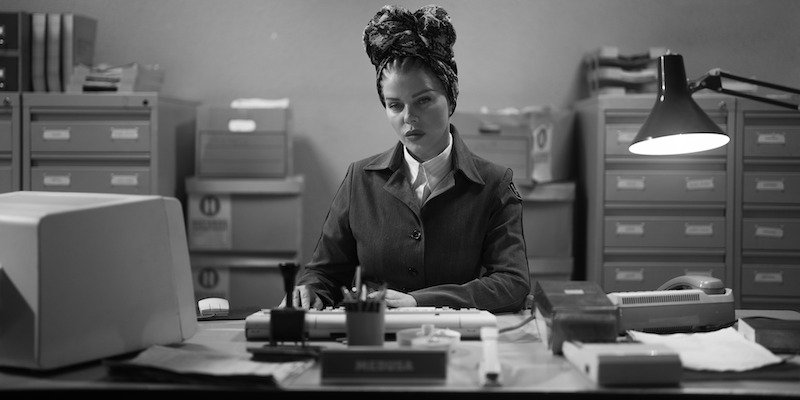 Black and white image of Debi Mazar as Medusa working at a desk in Season 1 of ‘Kaos’
