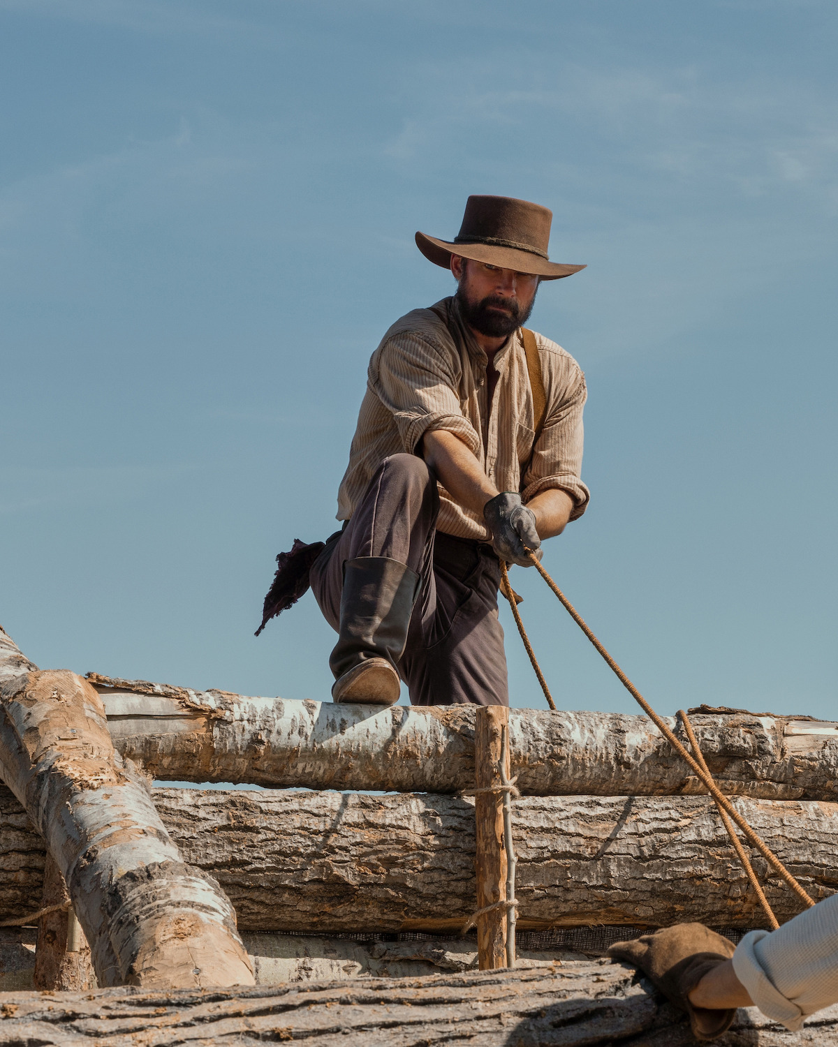 A man works on top of a pile of logs.