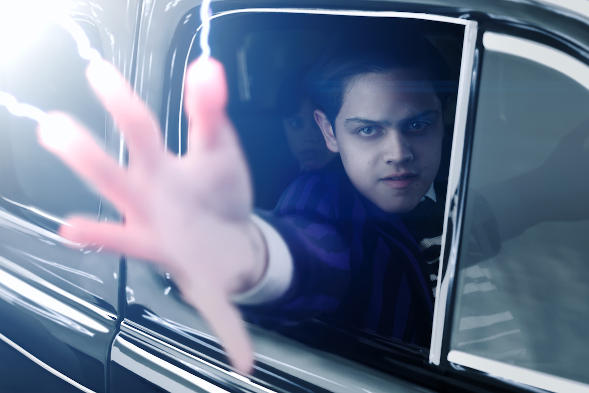Isaac Ordonez aș Pugsley Addams reaches through a car window as electricity shoots out of his fingers in Season 2 of ‘Wednesday’