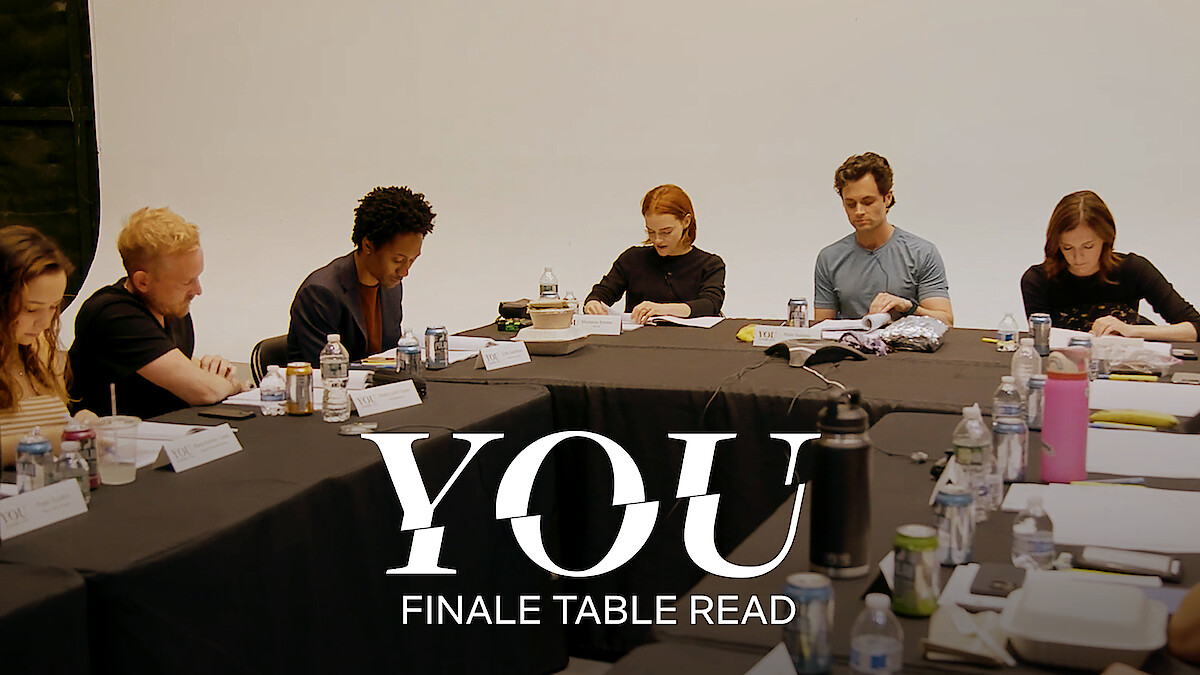 The cast of You Season 5 sitting around a large table with scripts, engaged in a table read.