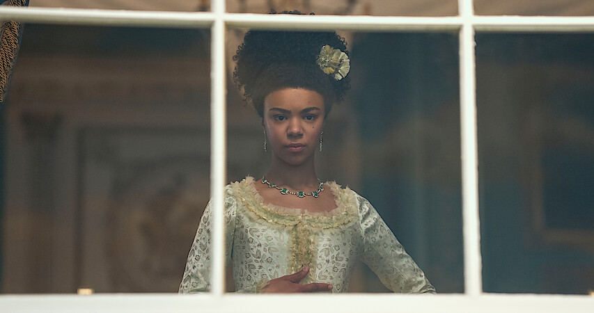 queen charlotte stands in front of a window thinking 