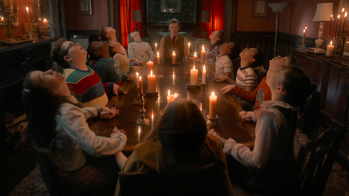 Jamie Campbell Bower as Henry Creel and a group of kids sit around a candlelit table in a dim room in 'Stranger Things 5'