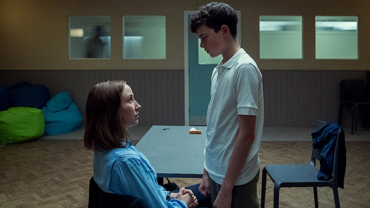  A woman sits in a chair with a teenage boy standing over her