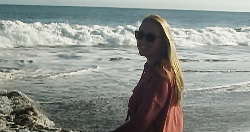 Woman sitting on beach, looking at camera.