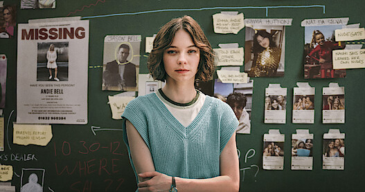 Emma Myers as Pip stands infront of a chalkboard covered in suspect photos and clue clippings in Season 1 of 'A Good Girl's Guide to Murder'
