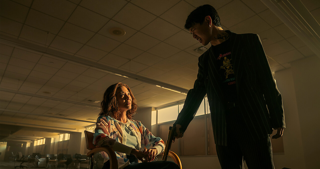 Michelle Yeoh as Mama Sun sitting in an empty room with an armed interrogator in 'The Brothers Sun.'