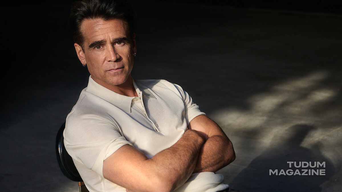 Colin Farrell leans back in a rolling chair in a white polo and black pants.