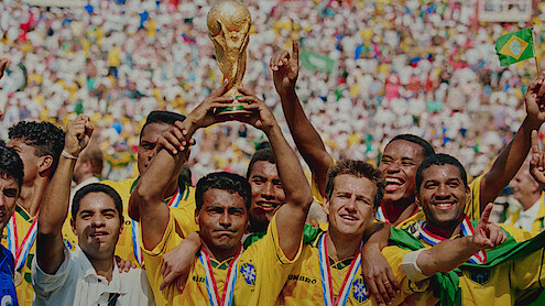 A player on Brazil's 1994 World Cup team holding up the World Cup Trophy with his teammates standing next to him.