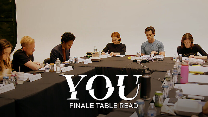 The cast of You Season 5 sitting around a large table with scripts, engaged in a table read.