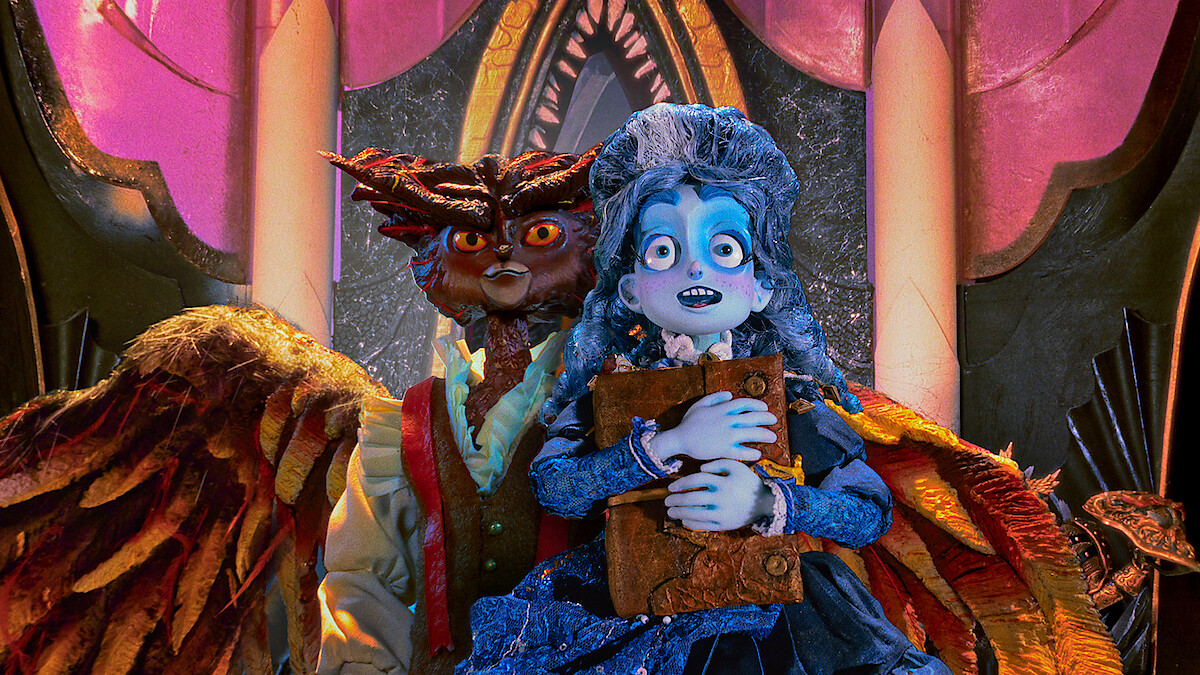 A blue-skinned, animated girl in a blue dress holds a book, standing nervously in front of a menacing owl-like creature with wings inside a lavish, ornately decorated room with pink and gold arches and dramatic lighting.
