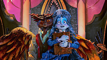 A blue-skinned, animated girl in a blue dress holds a book, standing nervously in front of a menacing owl-like creature with wings inside a lavish, ornately decorated room with pink and gold arches and dramatic lighting.