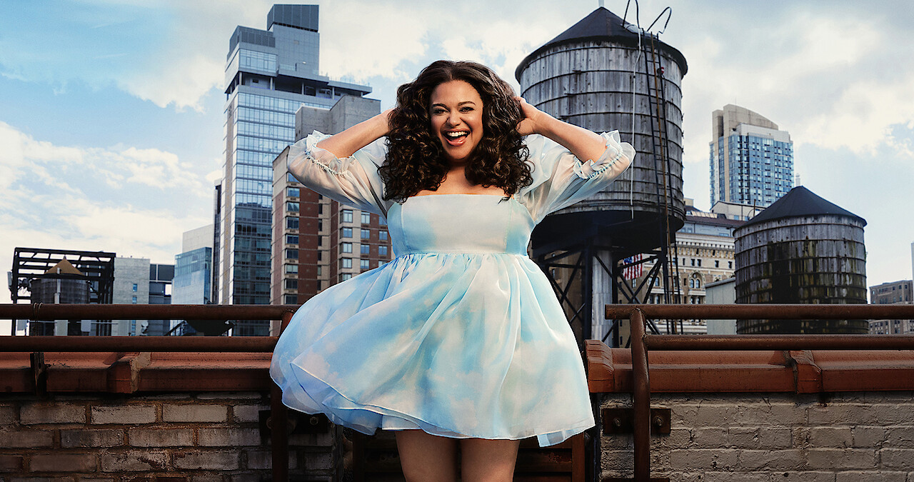 Michelle Buteau wears a bright, blue dress jacket and laughs.