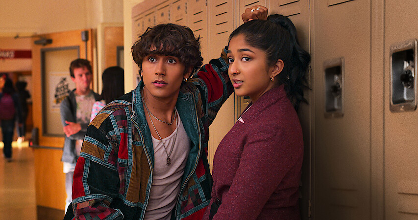 Michael Cimino as Ethan and Maitreyi Ramakrishnan as Devi in Never Have I Ever Season 4 standing against lockers.