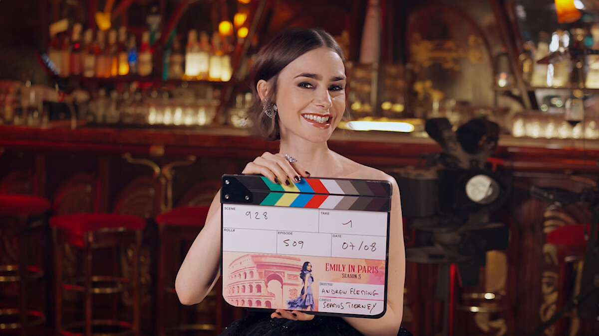 Lily Collins holds a film clapperboard labeled 'Emily in Paris'