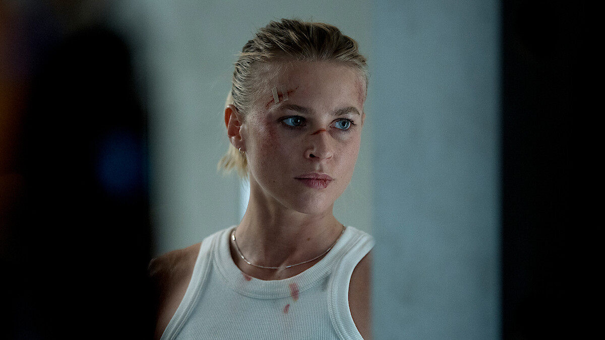Jeanne Goursaud stands in close up with bloody cuts on her face and blood spots on her white tank top in an image from 'Exterritorial.'