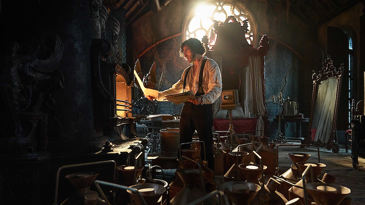A man studies papers in a dark, ornate room filled with scientific equipment and warm, dramatic light streaming through a stained-glass window, creating a mysterious and intense mood.