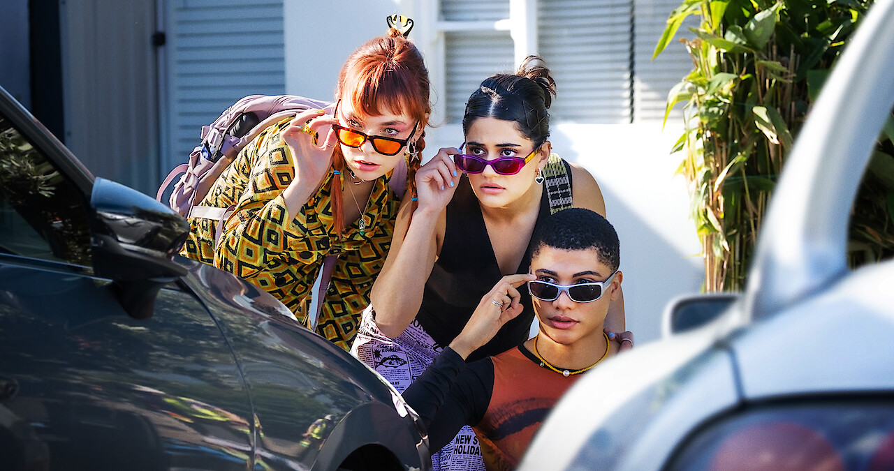 Three teems hide behind a car peeking over their sunglasses in Season 2 of 'Heartbreak High' 