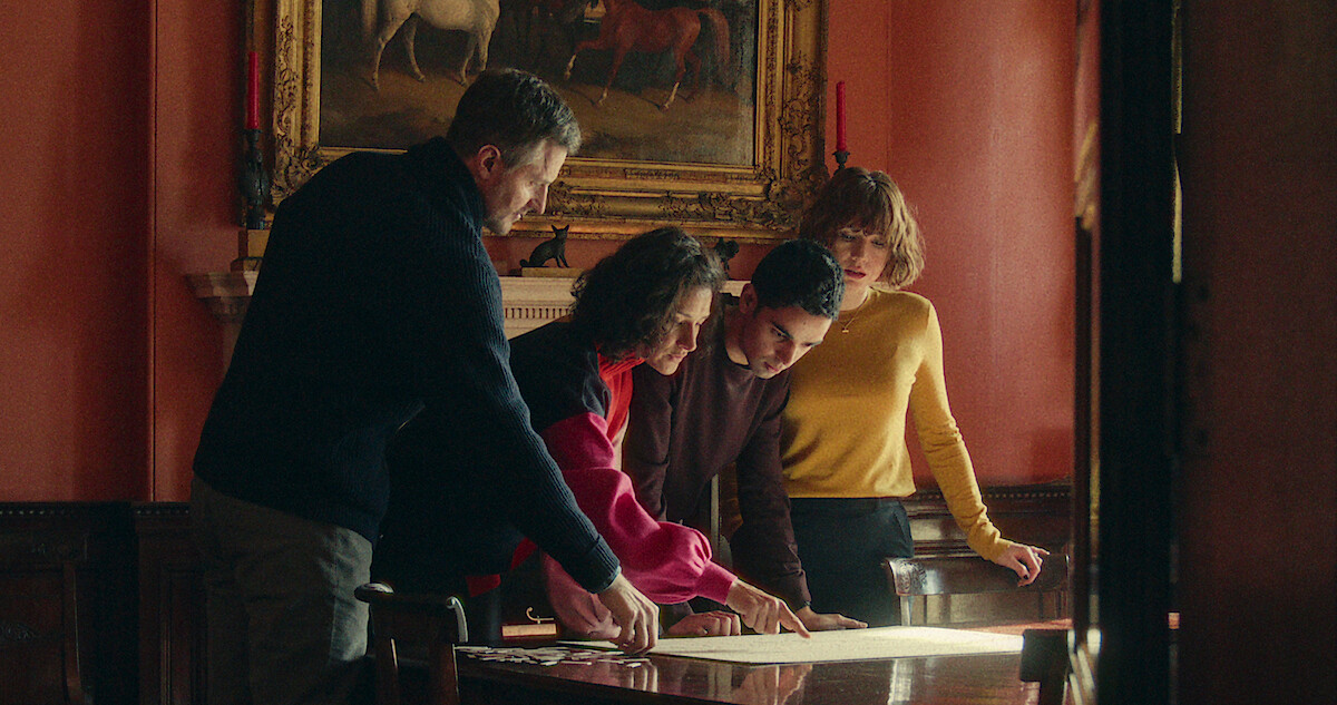 Three people standing around a desk in a pink room with a painting