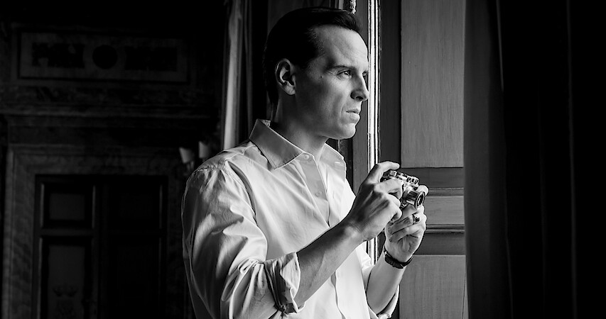 Black and white photo of Andrew Scott as Tom Ripley holding a camera while looking out of a window in Season 1 of 'Ripley'