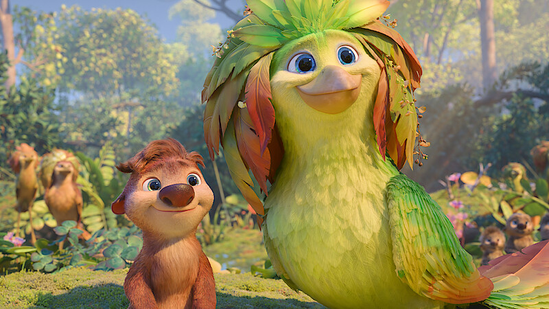 Animated scene with a smiling furry animal and a large colorful bird standing together in a vibrant, sunlit forest filled with foliage and other animal characters in the background.