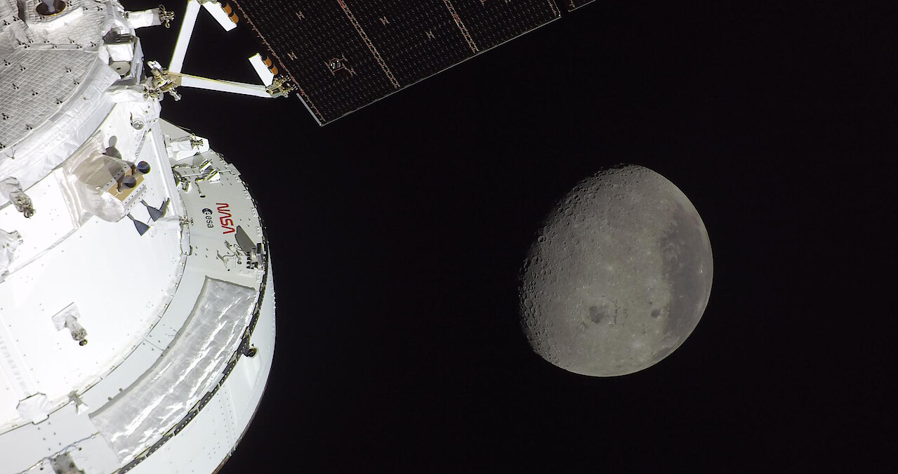 Part of a spacecraft in space with solar panels visible, and the moon in the background against the blackness of space.