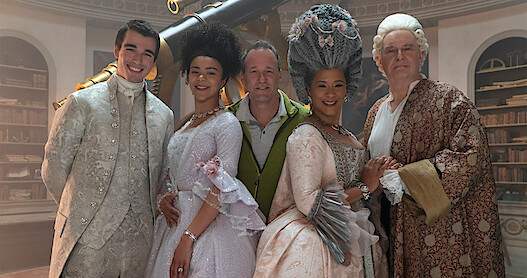 The young and older versions of Queen Charlotte and King George smile with director Tom Verica