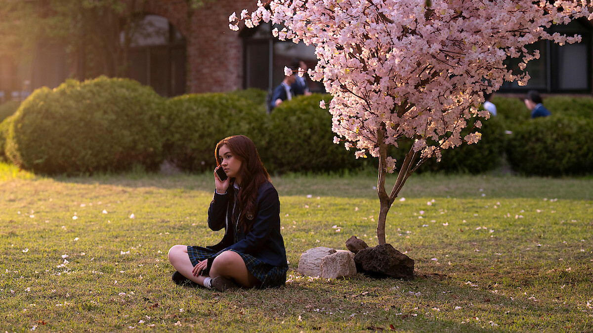 Anna Cathcart as Kitty Song Covey sits under a tree with pink blossoms in Season 2 of 'XO, Kitty' 