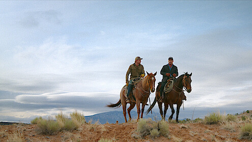 2 men on riding horses in the open terrain
