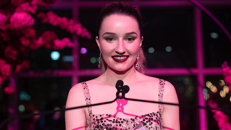Kaitlyn Dever as Belle smiles at a podium in 'Apple Cider Vinegar'