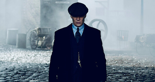 A close up image of Tommy Shelby in a cap, coat and suit in 'Peaky Blinders'