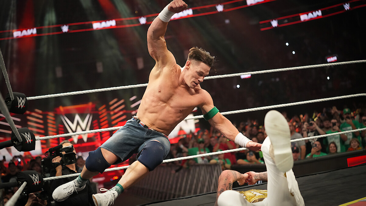 A wrestling match in a packed arena with a muscular wrestler mid-air attacking an opponent on the mat, energetic crowd cheering, bright lights, intense and action-packed atmosphere.
