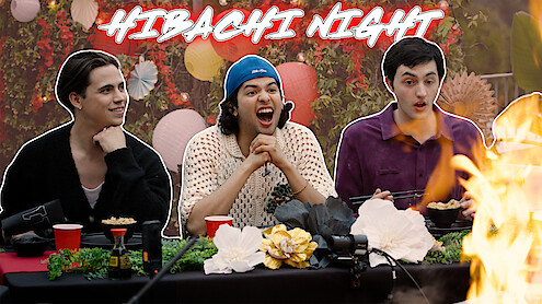 From left to right, Tanner Buchanan, Xolo Maridueña, and Gianni DeCenzo are seated at a dinner table, with flames rising dramatically on the right side.