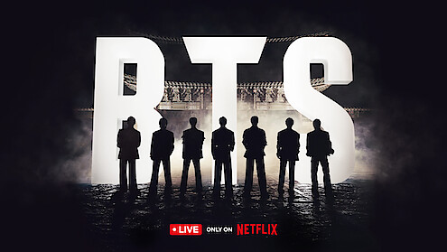 BTS standing silhouetted against giant 'BTS' letters