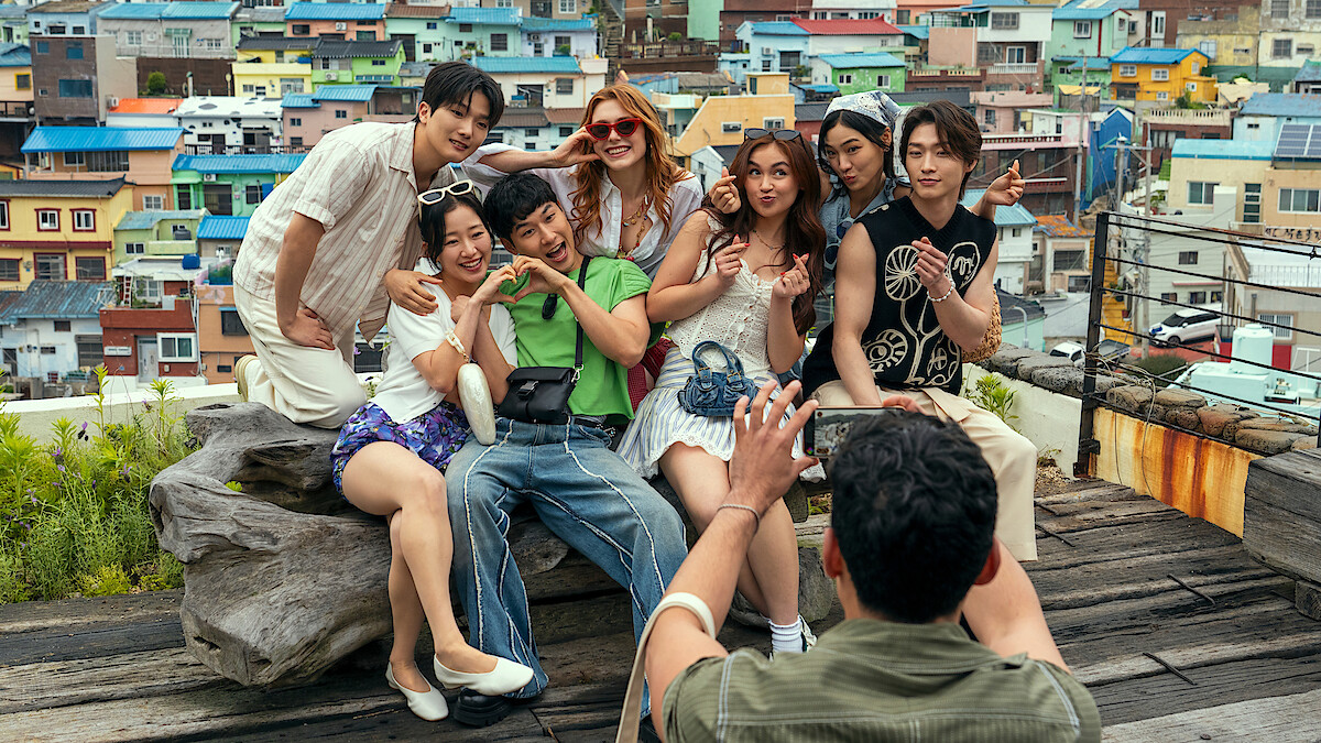 A group of friends poses happily for a photo on a rooftop with colorful houses in the background, showing a lively urban setting and cheerful atmosphere.