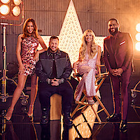 Chrissy Teigen, Jelly Roll, Sarah Michelle Gellar, and Anthony Anderson pose on a glossy studio floor with large movie lights and a star prop behind them, creating a glamorous and celebratory entertainment show setting.