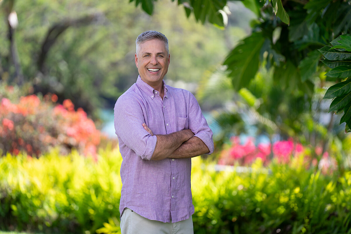 Mark L. Walberg standing with his arms crossed in a garden.